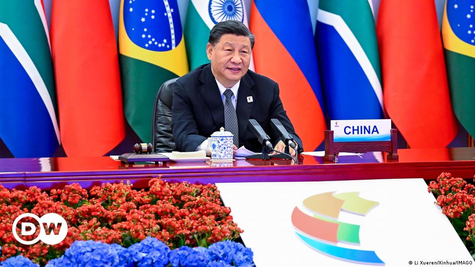 One man stands in front of a Brazilian flag, another in front of a Russian flag, both in side profile.