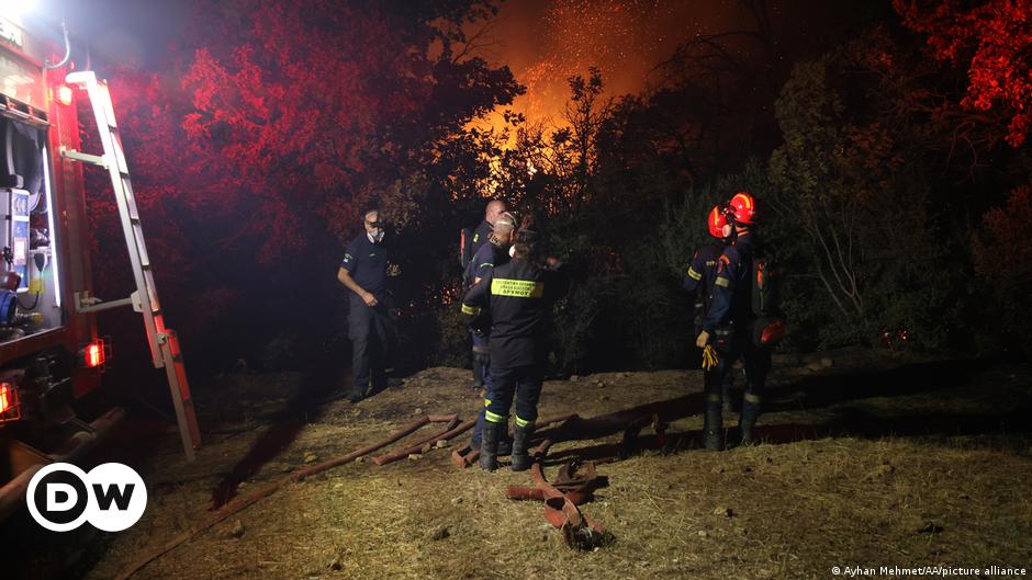 Firefighters stand next to a wildfire as they work to extinguish it