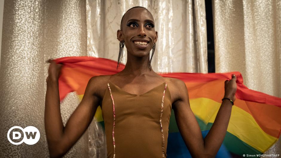 A man holds a rainbow flag in front of his face