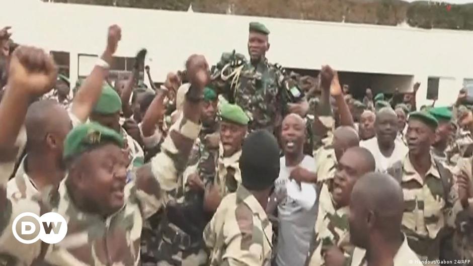A group of men wearning military uniforms stand solemnly in a row as a spokesperson speaks into a microphone