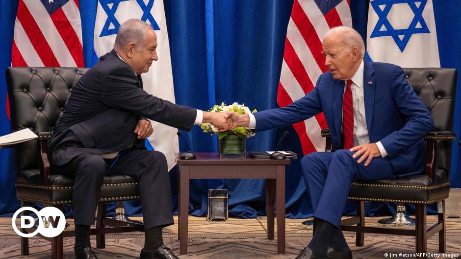 The Israeli flag draped on a flag pole in front of a white building with six windows