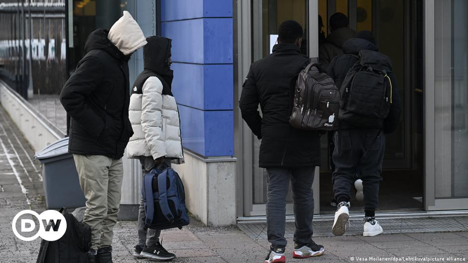 Soldiers in camouflage, a border agent in black and a migrant wearing a white jacket and standing next to a bicycle at the Russian-Finnish border