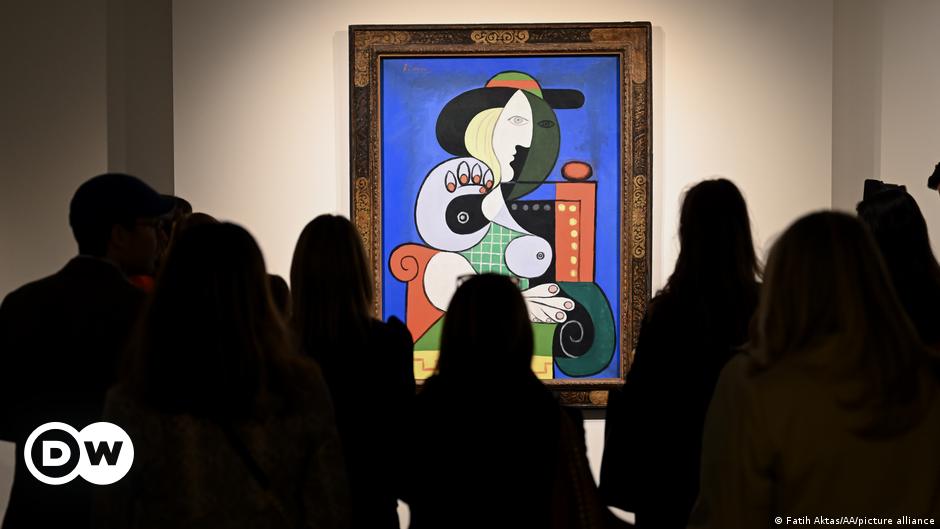 People on a rock structure looking at a poster with a picture of Pablo Picasso.
