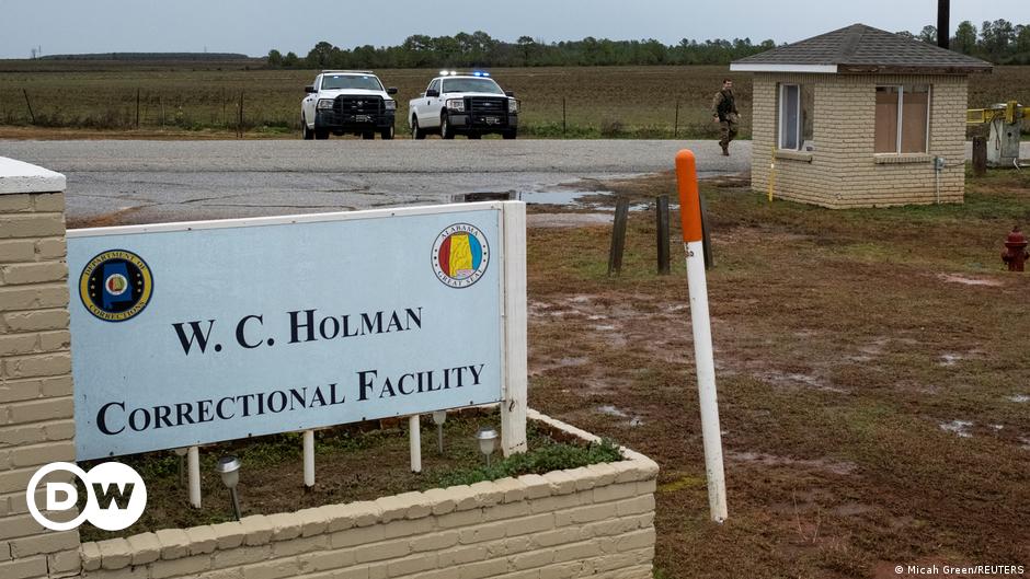 A view of several empty nooses hanging against a darkening sky, with a row of silhouettes of people standing in the background