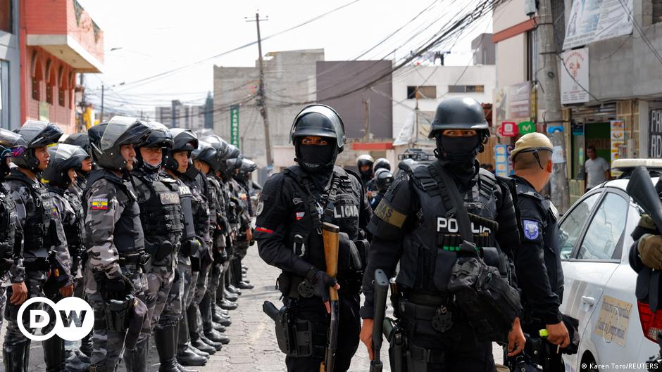 Armed soldiers in camouflage stand in front of a graffiti-covered wall