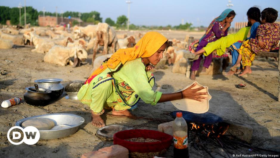 A man with a gray beard talks into a cellphone in front of a wall of screens