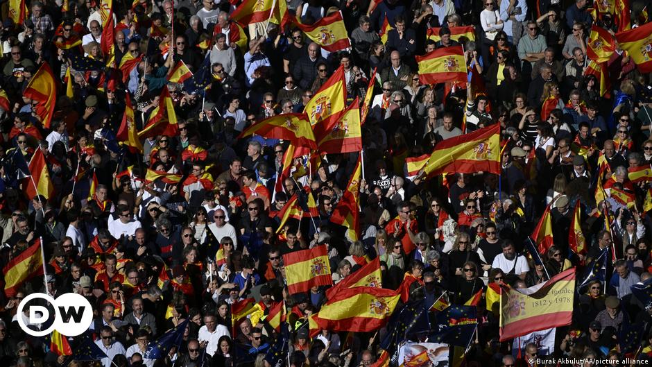 Protesters waving Spanish and EU flags in Madrid, with an extra-large Spanish flag waving tall in the center